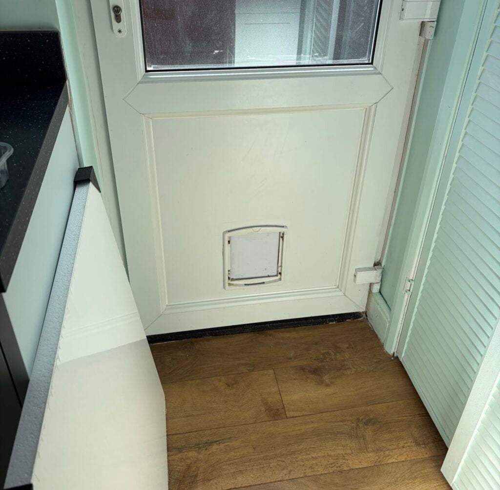 Small cat flap fitted into the lower panel of a white UPVC door