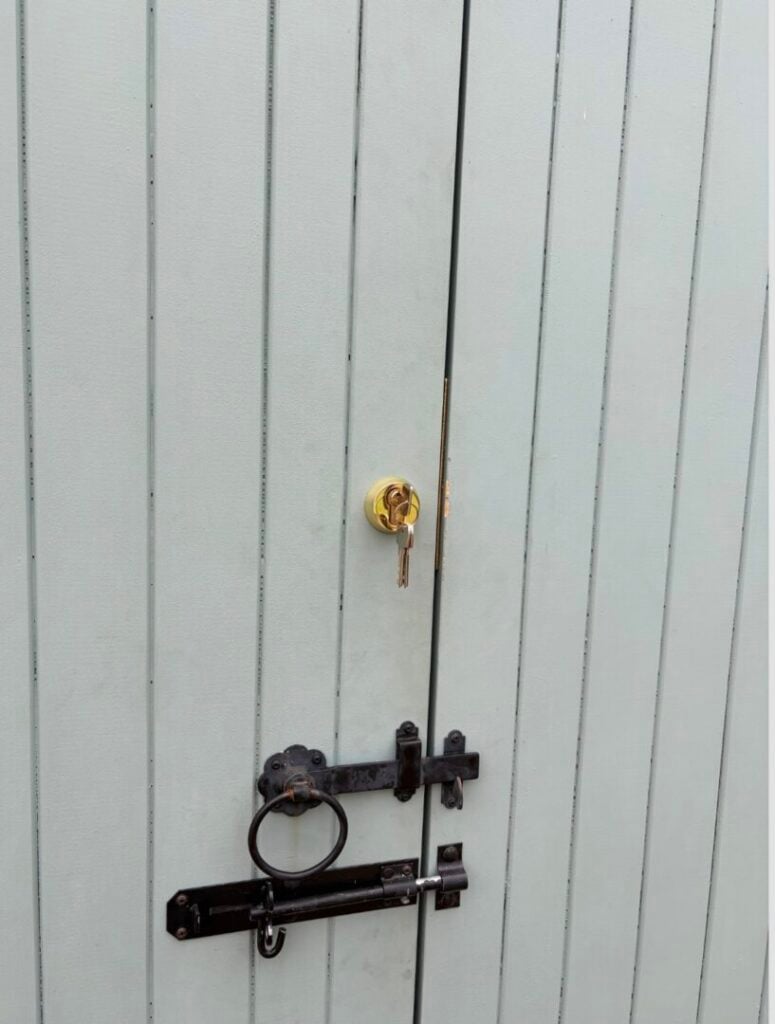 Keys in a brass lock on a painted timber gate with black latch and bolt