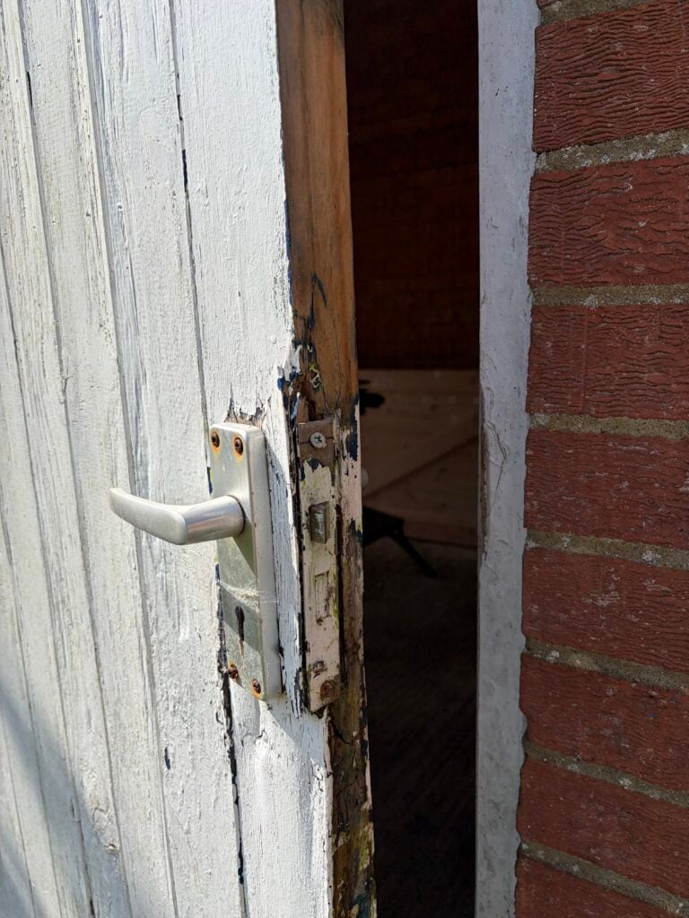 Worn lock and silver handle on a timber door with peeling white paint