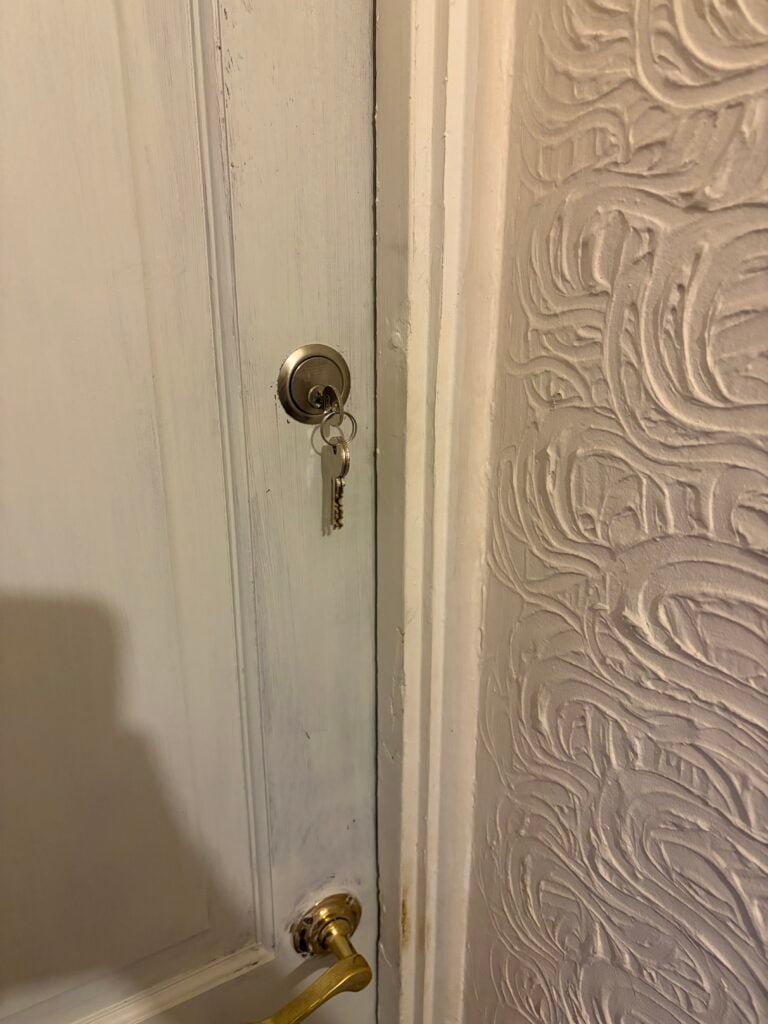Keys in a cylinder lock above a brass handle on a white door