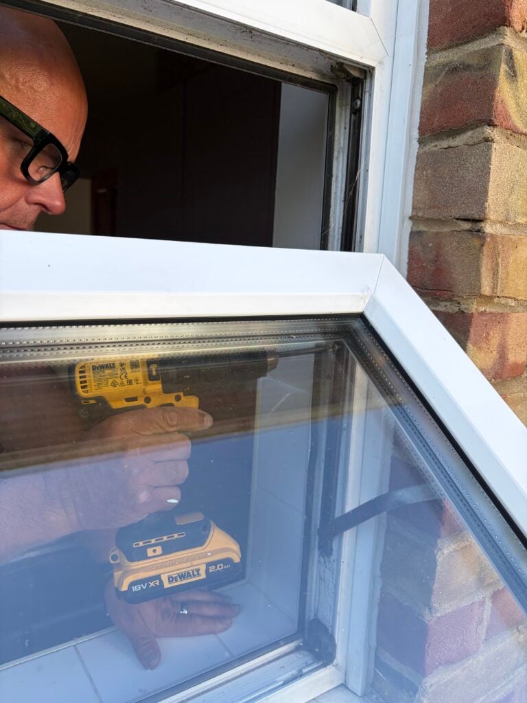 Technician working with a cordless drill behind an open UPVC window
