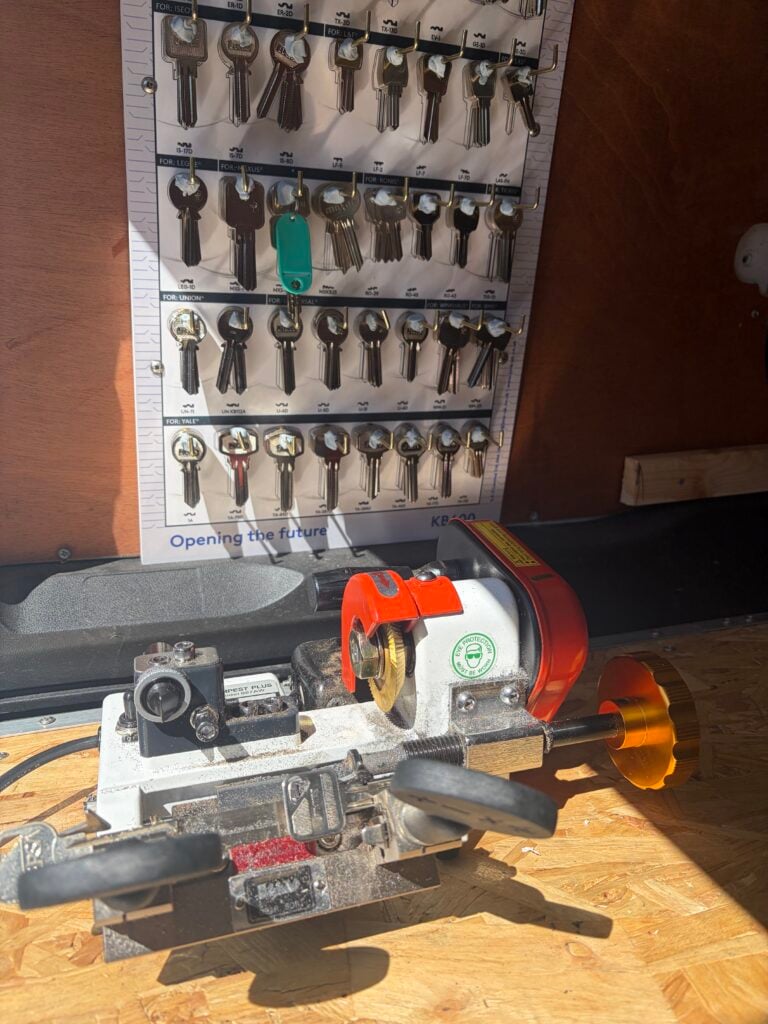 Key cutting machine on a workbench beneath a rack of key blanks
