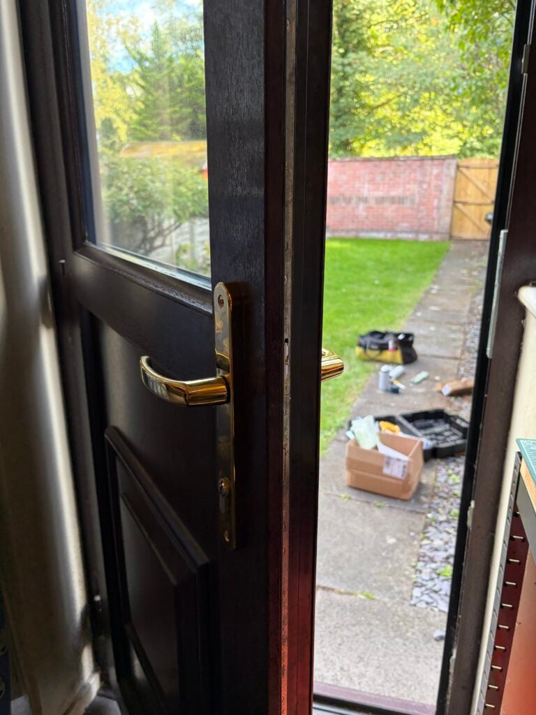 Gold-coloured lever handle and lock on an open woodgrain glazed door