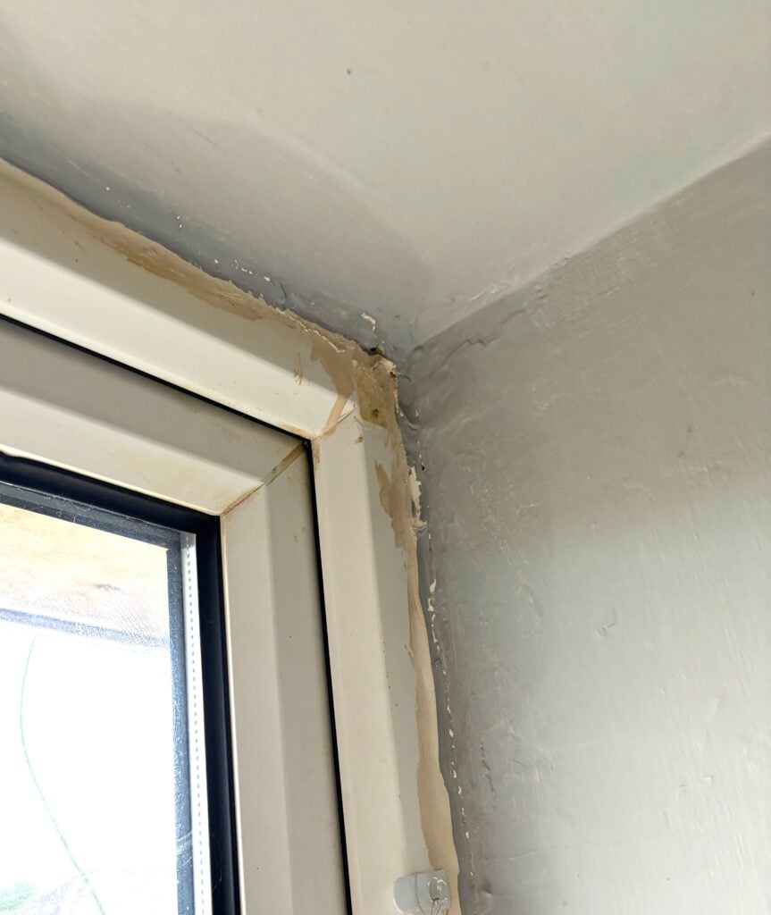 Upper corner of a white UPVC window and surrounding wall