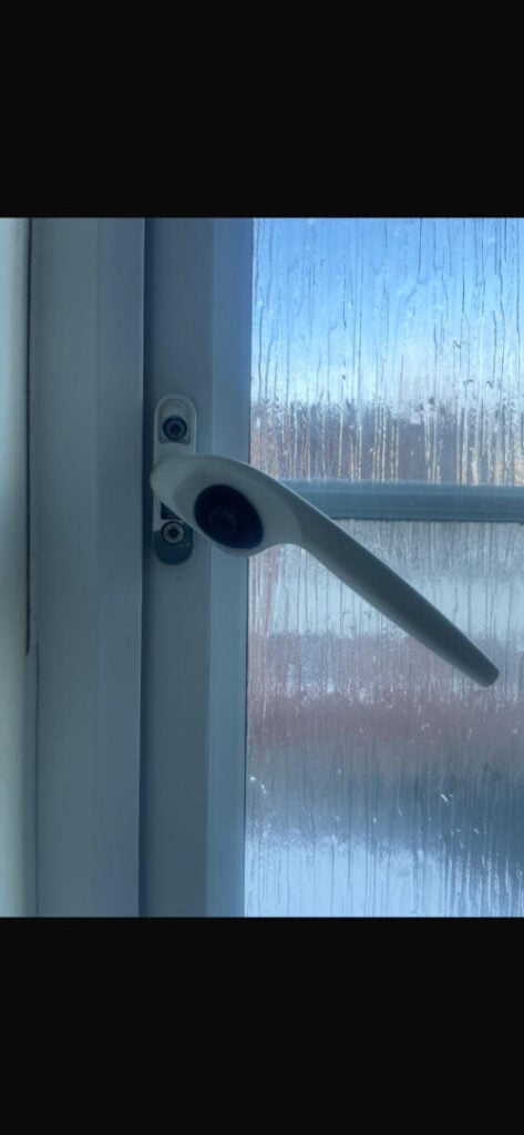 Angled white window handle with its fixing screws exposed